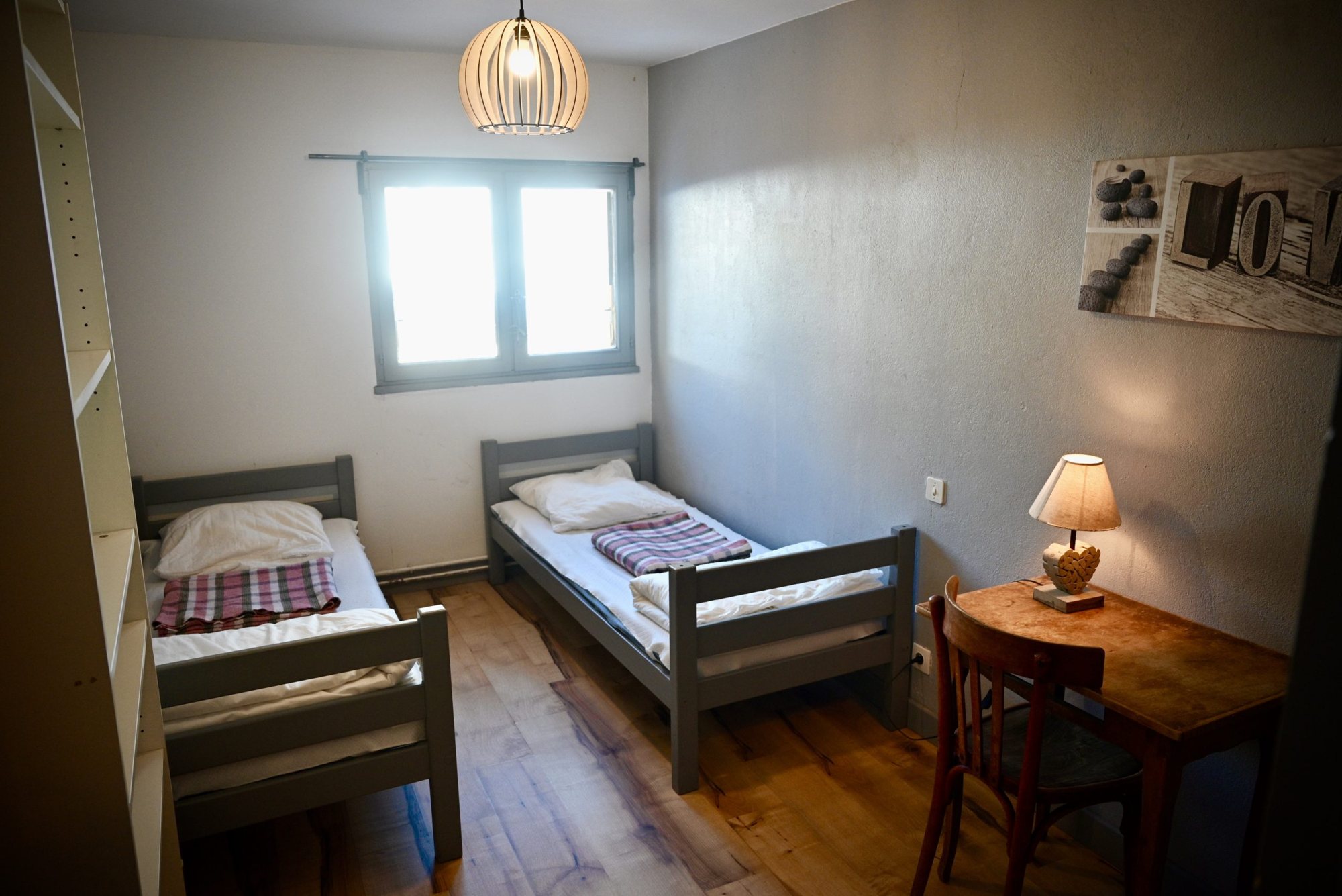 Chambre simple avec deux lits gris et bureau en bois