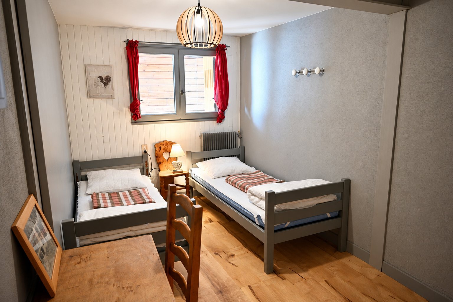 Chambre simple avec deux lits gris et parquet en bois