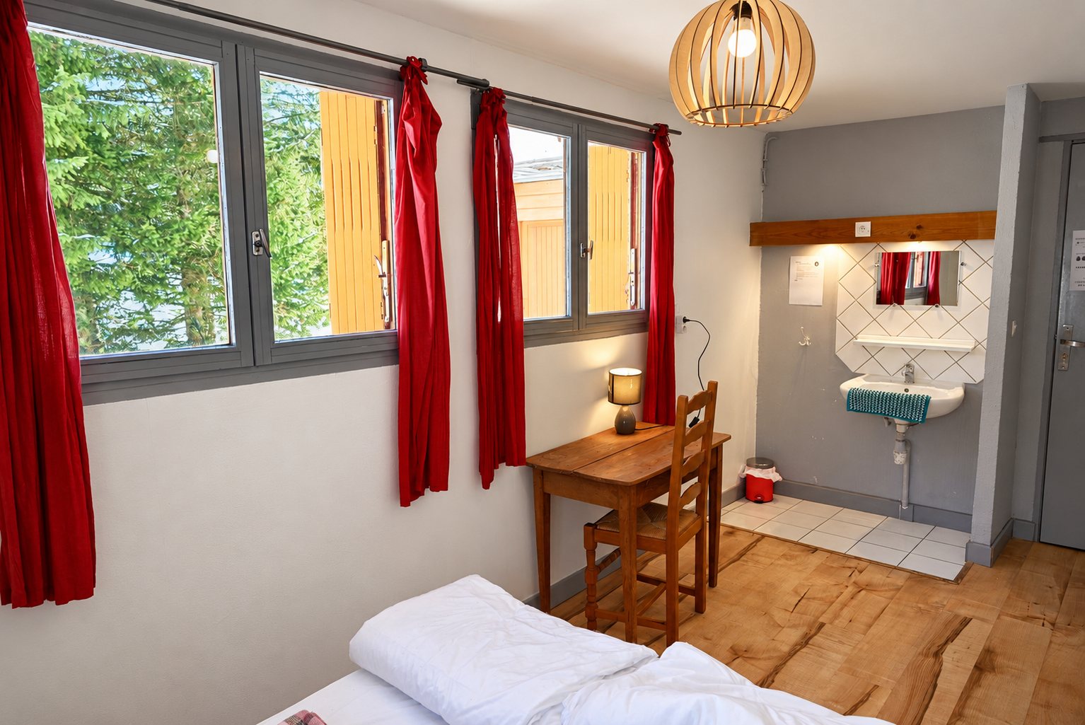 Chambre simple avec rideaux rouges, bureau en bois et lavabo