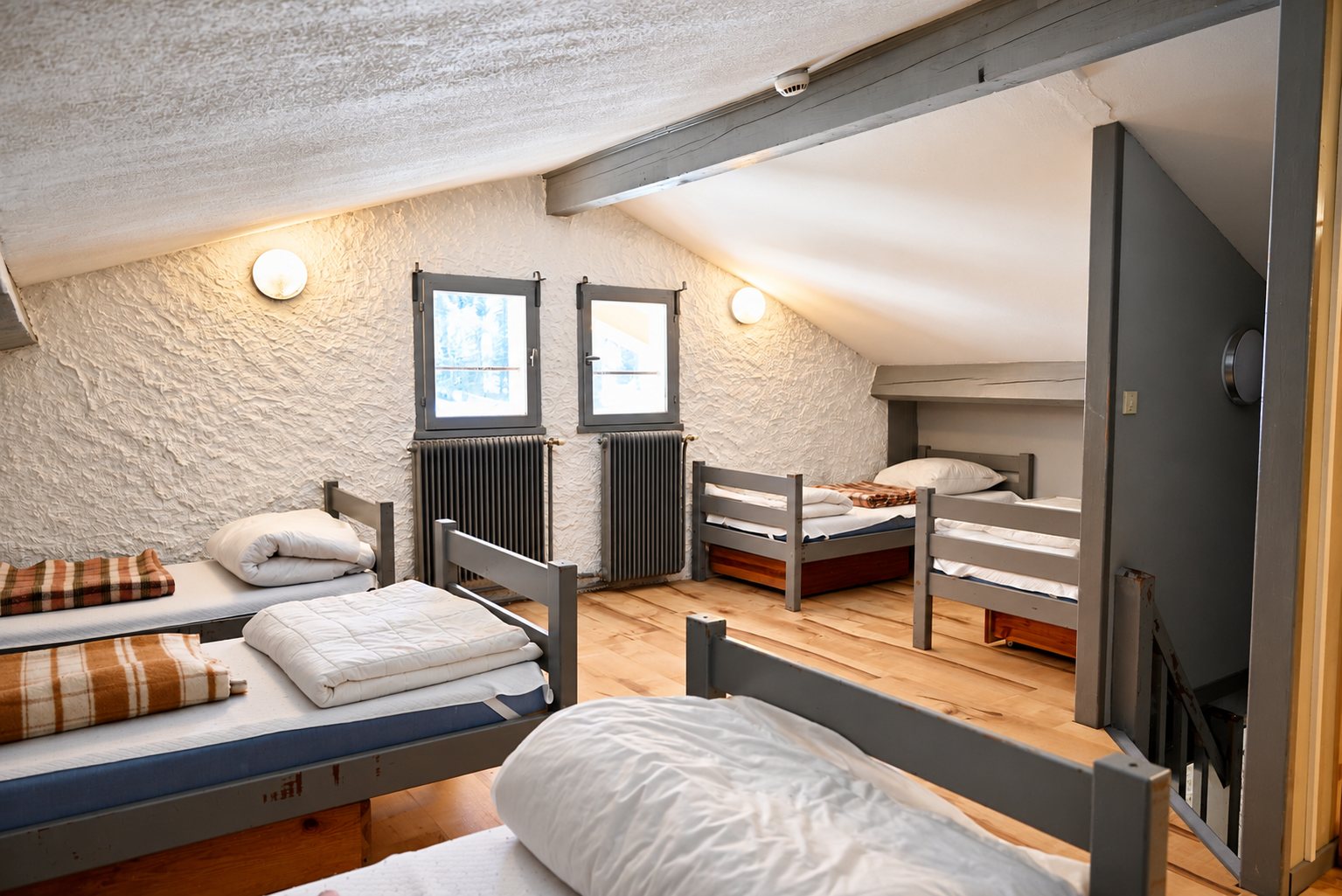 Dortoir sous les combles avec lits gris et parquet clair