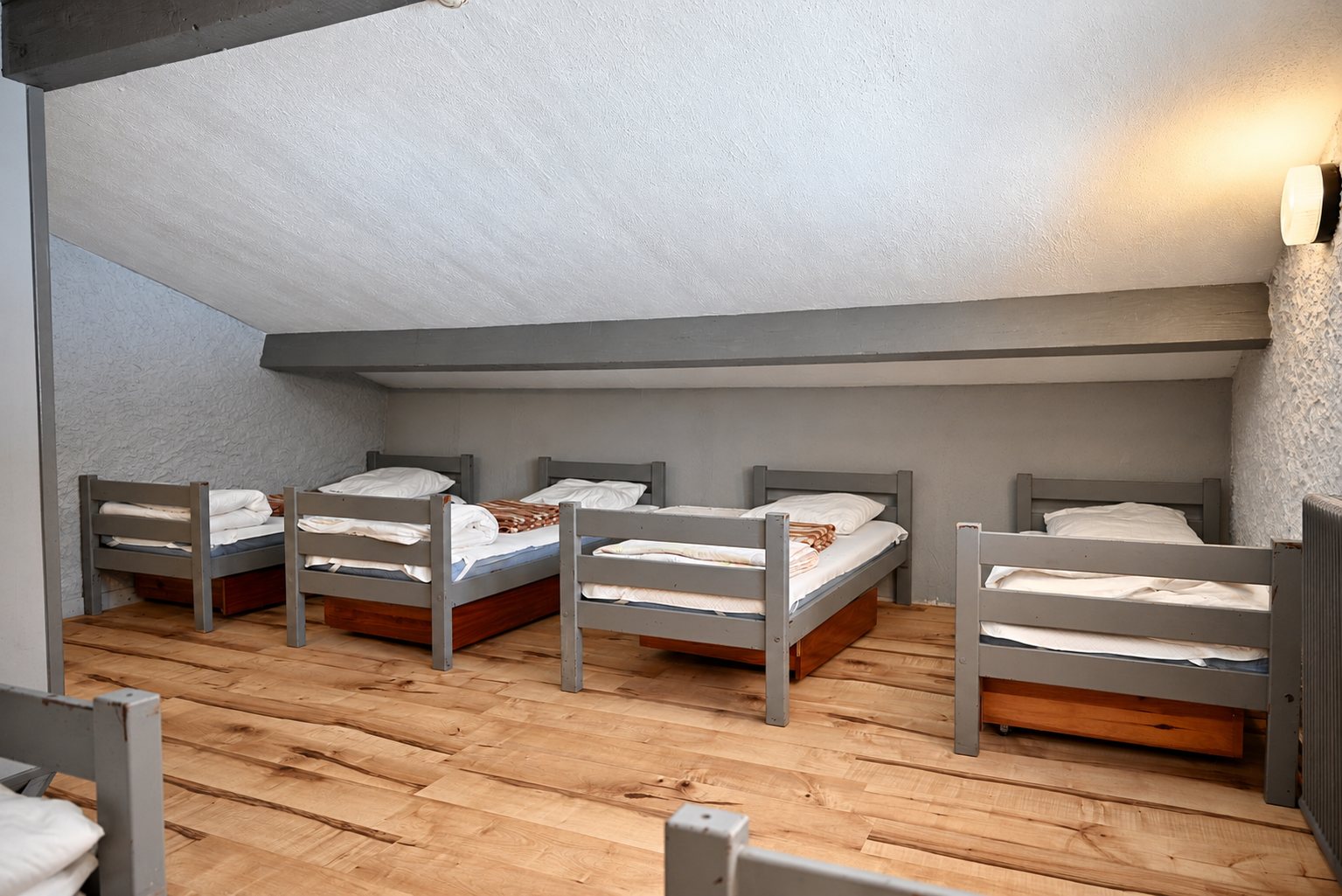 Dortoir mansardé avec lits simples gris et parquet clair