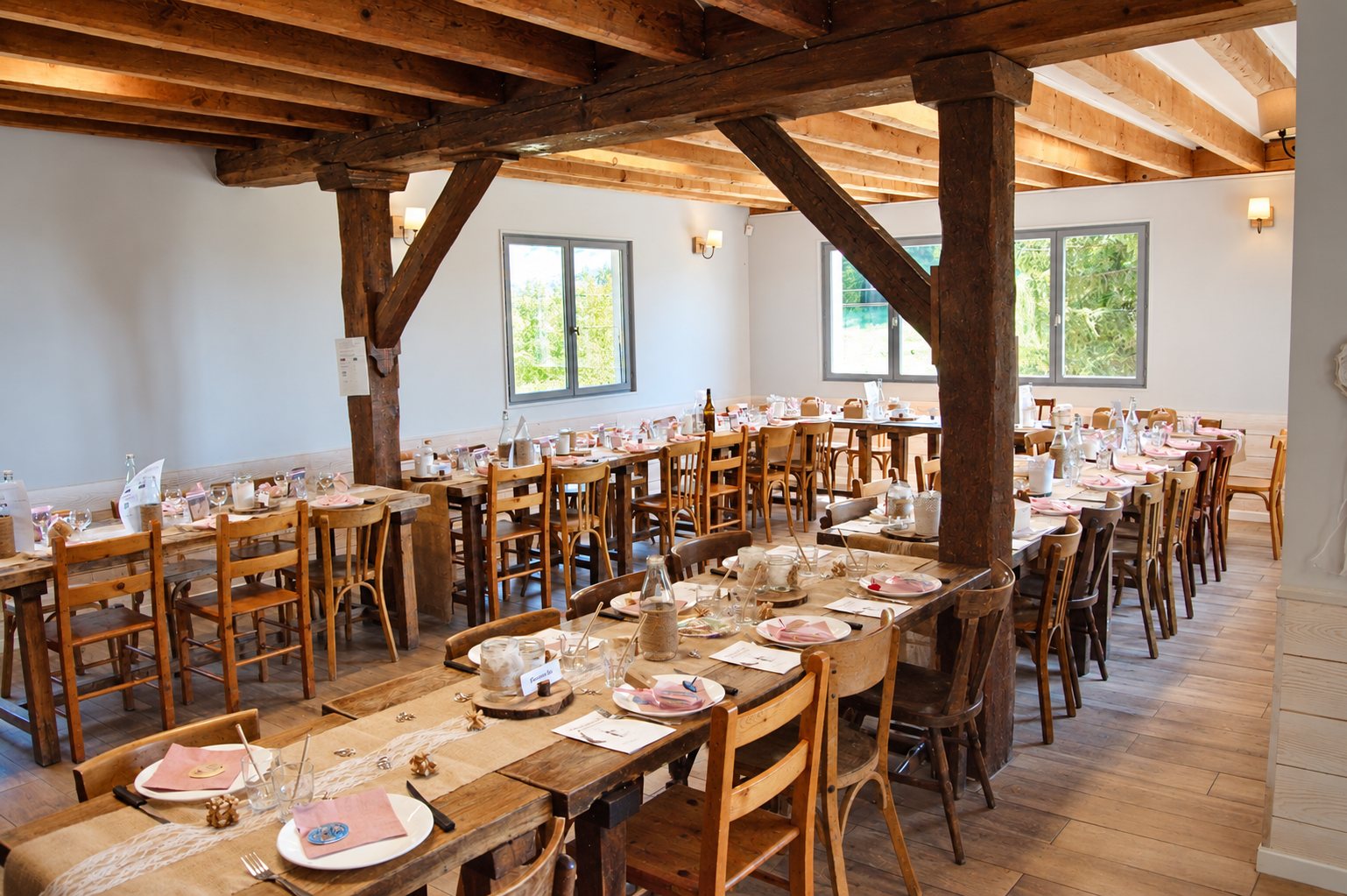 Salle à manger du gîte avec de longues tables dressées sous les poutres